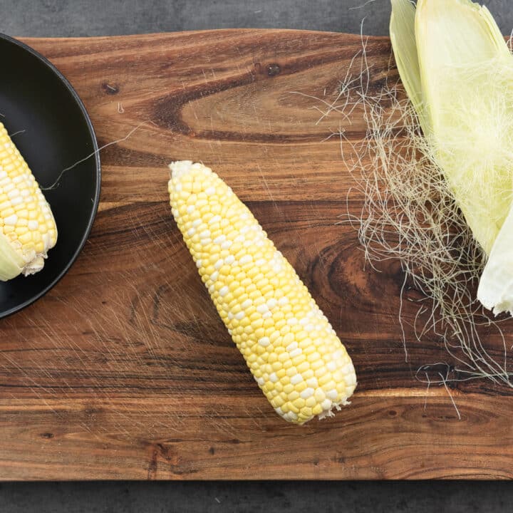 A corn on the cob on a wooden board with husk and silk removed.