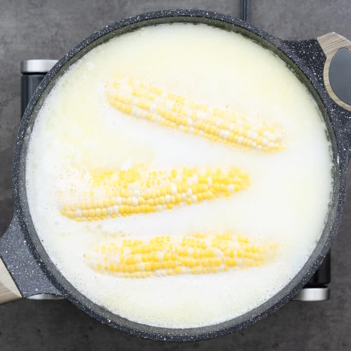 A pot with corn on the cob boiling in a mixture of milk and butter.