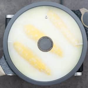 Corn on the cob is simmering in a pot with a covered lid.
