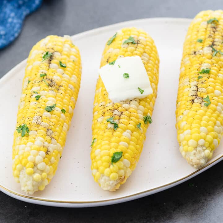 A white tray with corn on the cob seasoned with salt, pepper, and butter.