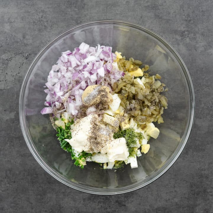 A glass bowl with egg salad ingredients.