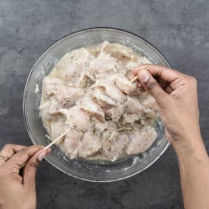 Showing marinated chicken threaded on a wooden skewer.