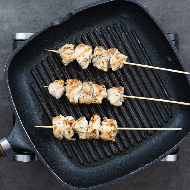 A grill pan with chicken on skewers grilling.
