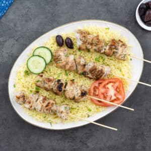 Chicken Souvlaki served over rice pilaf on white plate.