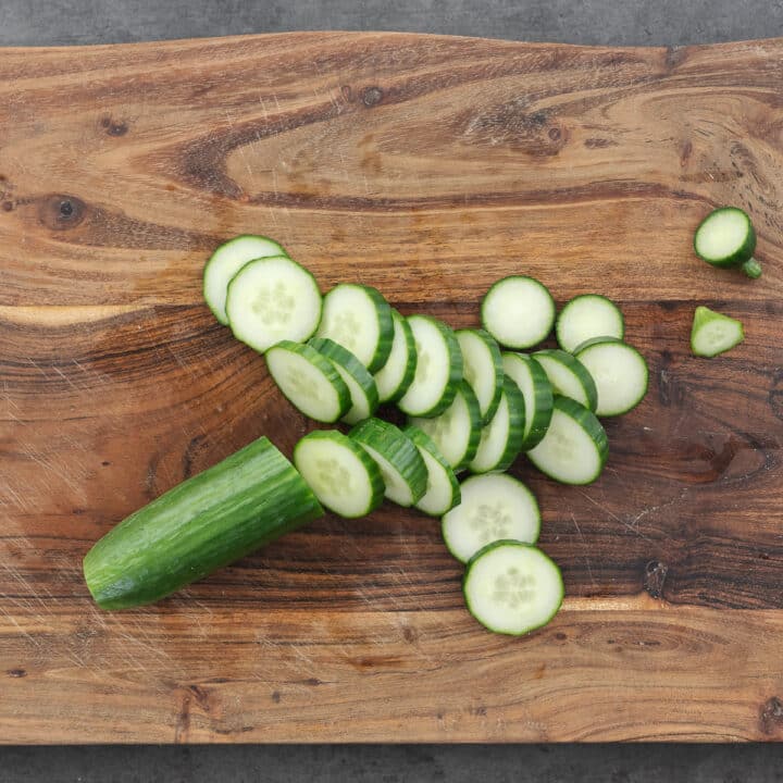 Wooden board with sliced cucumber.