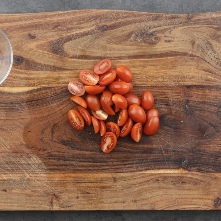 Wooden board with halved grape tomatoes.