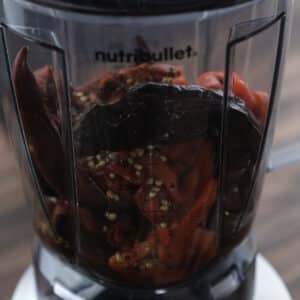 A blender jar on the blender with harissa ingredients ready for blending.