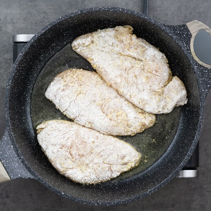 Chicken breasts coated in lemon pepper flour frying in a pan.