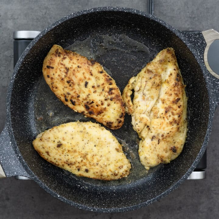 Pan-fried lemon pepper chicken breasts in a pan.