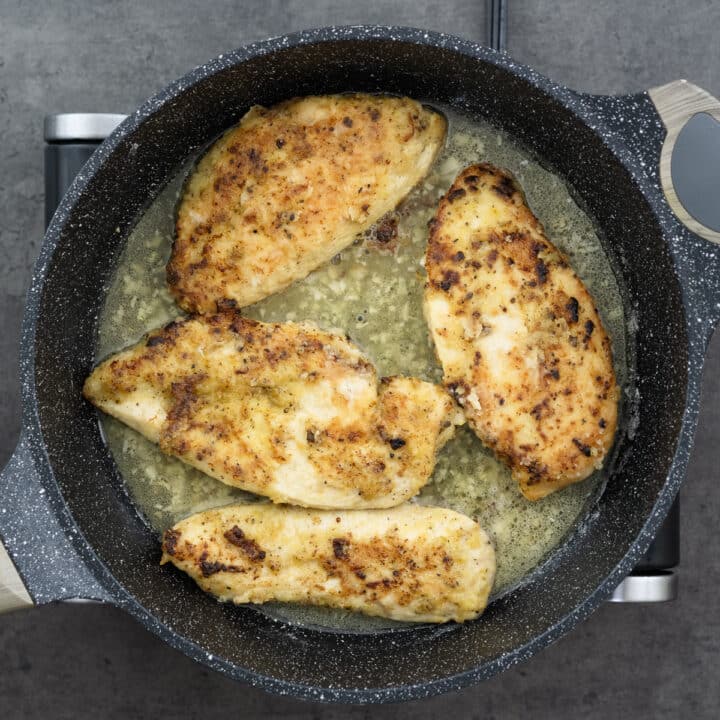 Lemon pepper chicken simmering in savory sauce in a pan.