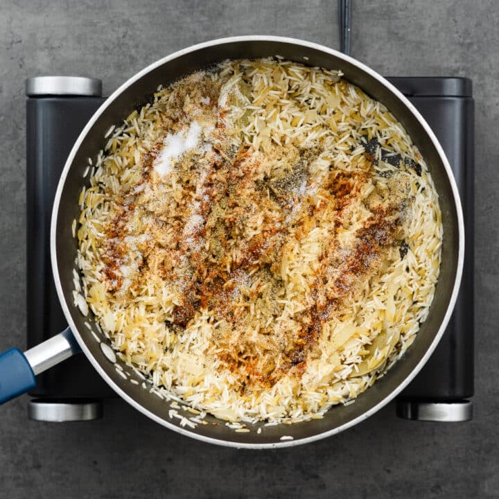 A pan with rice and orzo mixture seasoned with spice powders.