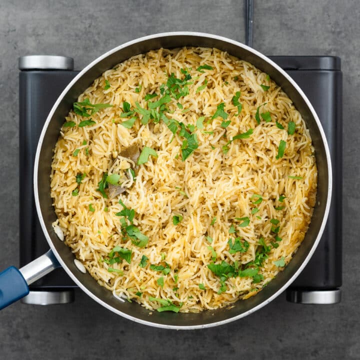 A pan with rice pilaf garnished with parsley leaves.