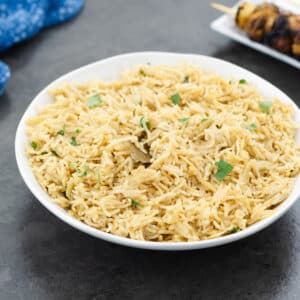 Rice pilaf served in a white bowl with chicken kabob alongside.