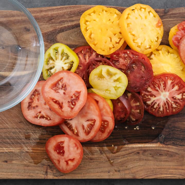 A rustic wooden board displaying sliced ripe tomatoes.