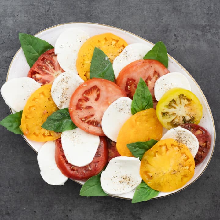 A beautifully assembled Caprese Salad, seasoned with salt, pepper, and a drizzle of olive oil.