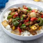 Chinese cashew chicken served in a white bowl with rice on a white table, surrounded by a blue towel, and a golden fork.