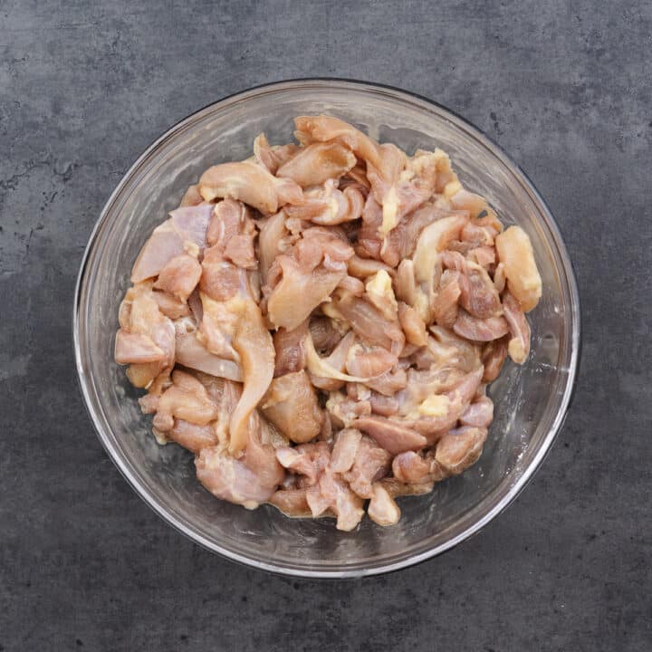 A bowl filled with marinated boneless chicken pieces.