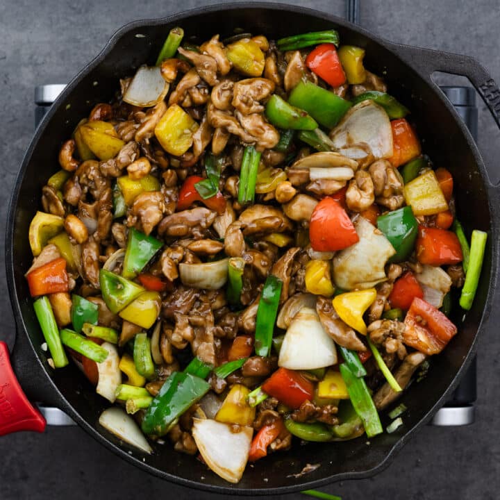 A cast iron pan with cashew chicken garnished with green onions.