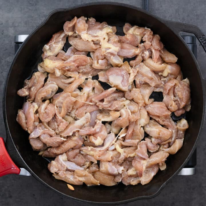 A cast iron pan with marinated chicken pieces.