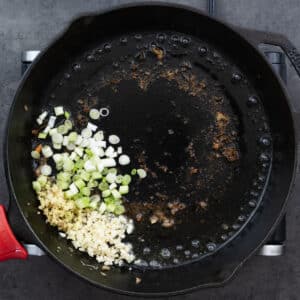 A cast iron pan with aromatics like ginger, garlic, and green onions.