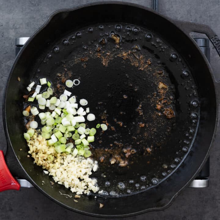 A cast iron pan with aromatics like ginger, garlic, and green onions.
