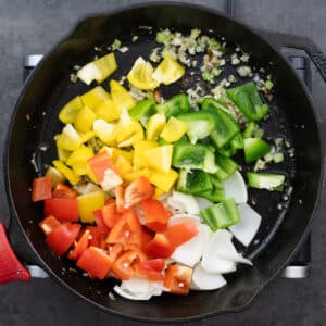 A cast iron pan with a mix of bell peppers and aromatics being stir-fried.
