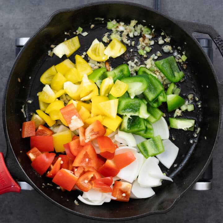 A cast iron pan with a mix of bell peppers and aromatics being stir-fried.