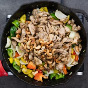 A cast iron pan with bell peppers, stir-fried chicken, and toasted cashews.