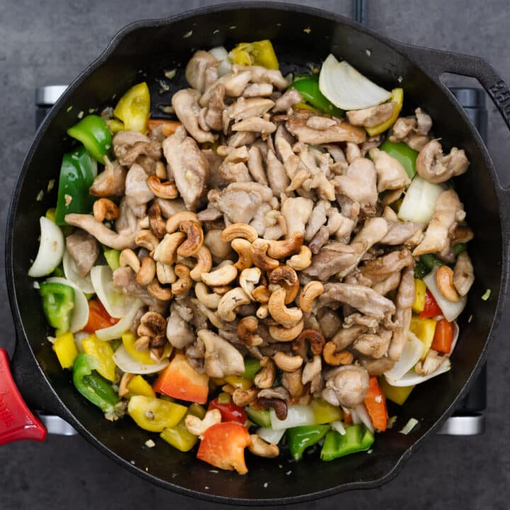 A cast iron pan with bell peppers, stir-fried chicken, and toasted cashews.