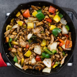 A cast iron pan with cashew chicken coated in stir-fry sauce.
