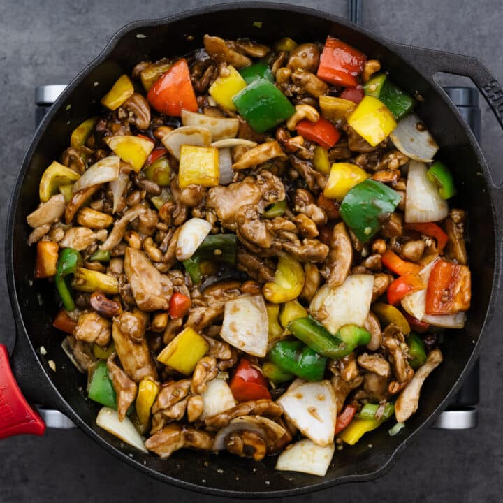 A cast iron pan with cashew chicken coated in stir-fry sauce.