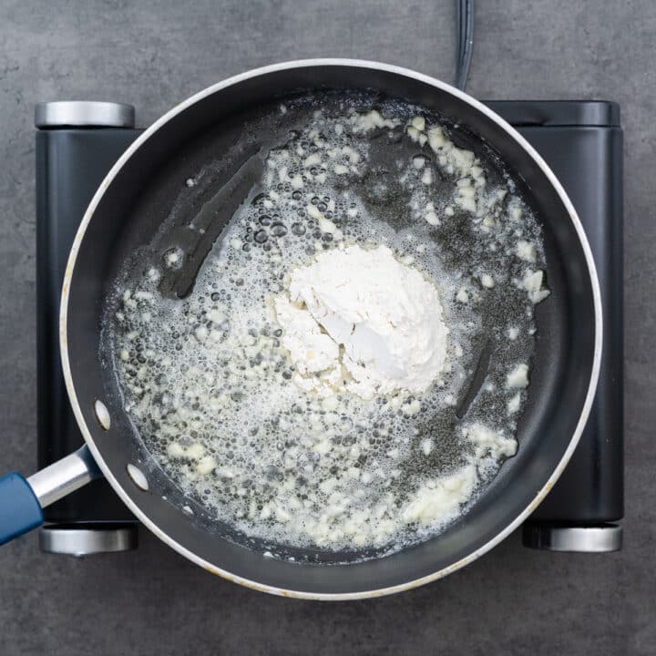 A pan with all-purpose flour being added to the garlic butter mixture, creating a roux.