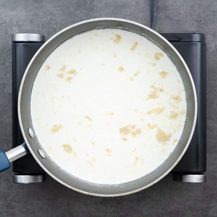 A pan with milk and heavy cream poured into the garlic flour mixture to form a creamy sauce.