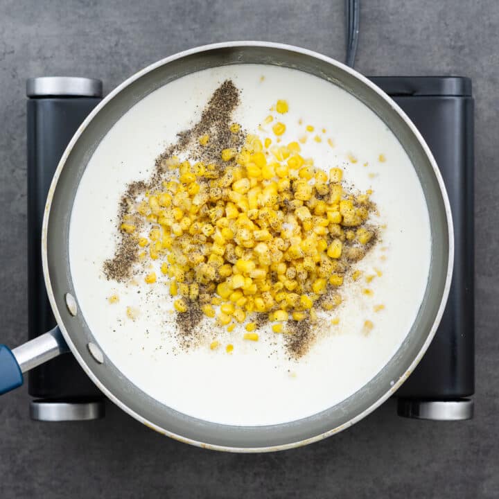 A pan with corn kernels and seasoning added into the milk and cream mixture.