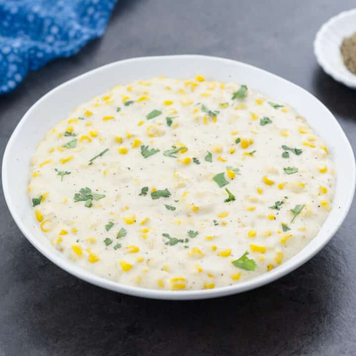 A bowl of creamed corn served and garnished with fresh parsley leaves, ready to enjoy.