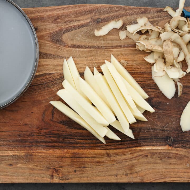 A wooden board with peeled and sliced potatoes for chips.