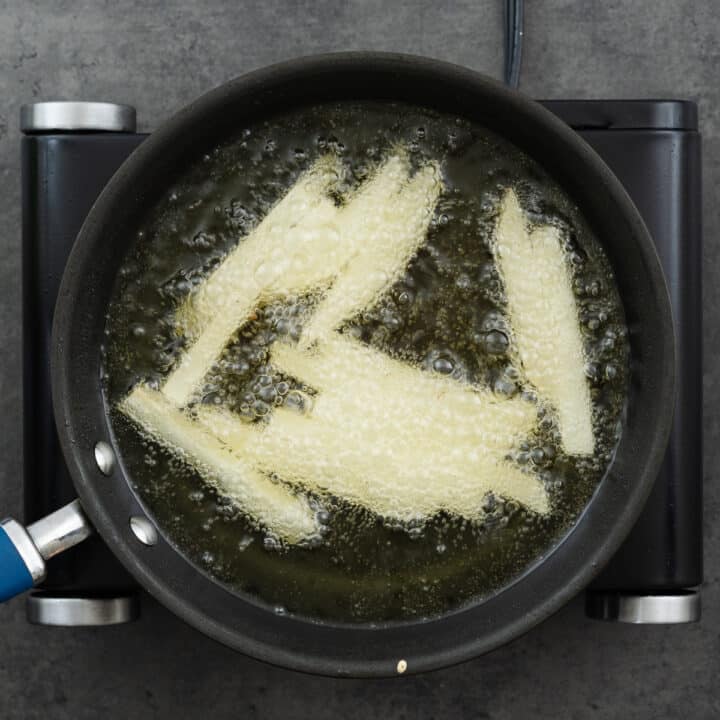 A pan with sliced potatoes for chips frying in oil.