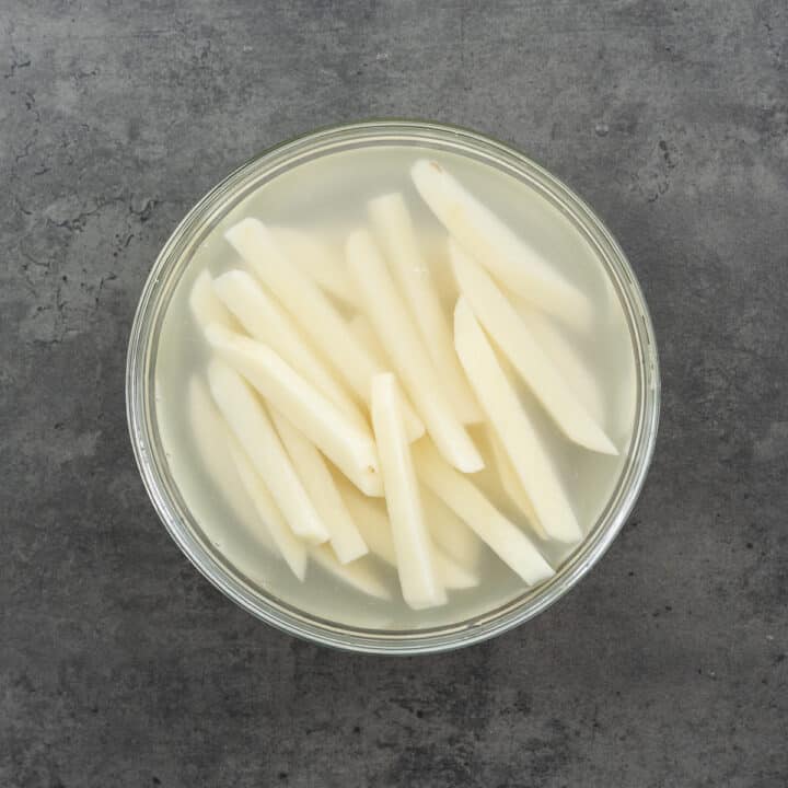 A bowl with sliced potatoes soaked in water for rinsing.