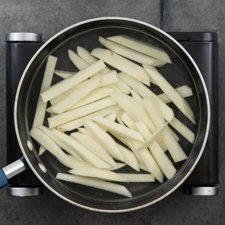 Sliced potatoes for chips blanching in a wide-bottom pan with water.