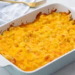 Baked mac and cheese in a white baking dish on a white table, with a white towel and a golden fork around it.