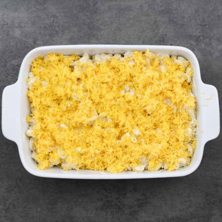 A baking dish filled with macaroni and cheese, topped with a layer of grated cheddar cheese.