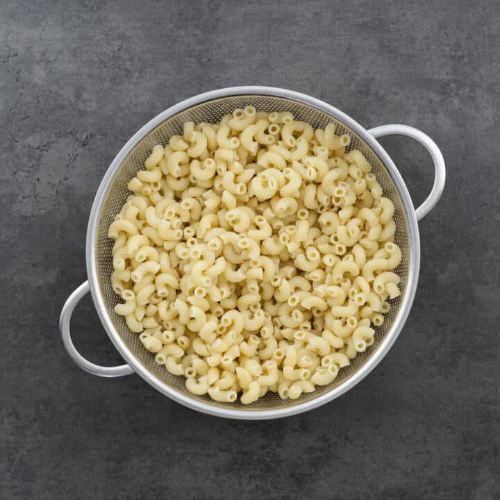 A colander filled with drained, cooked macaroni pasta.