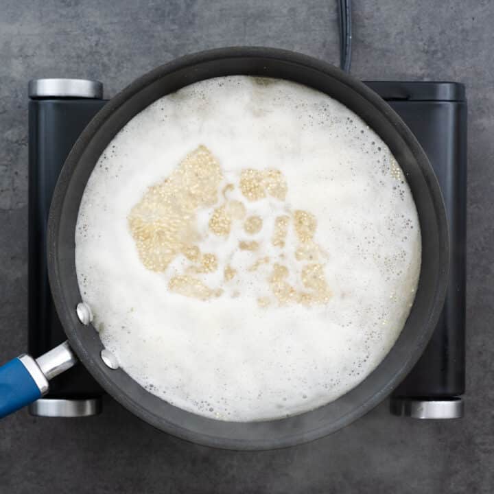 A pan with quinoa and water reaching a boil.