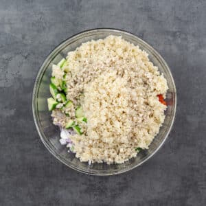 A bowl with layers of crisp vegetables, chickpeas, quinoa, and salad dressing.