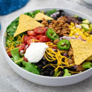 Homemade taco salad in a white bowl on a white table with a blue towel in the left corner.