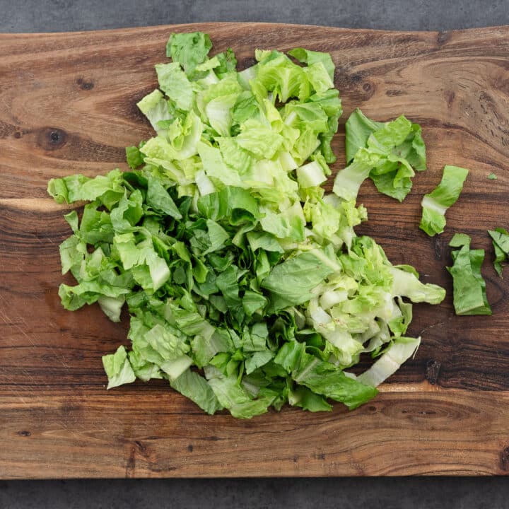 A wooden cutting board with chopped romaine lettuce.