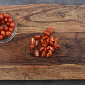 A wooden board with halved cherry or grape tomatoes.