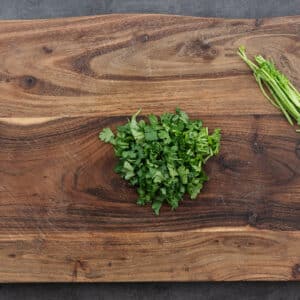 A wooden board with chopped cilantro leaves.