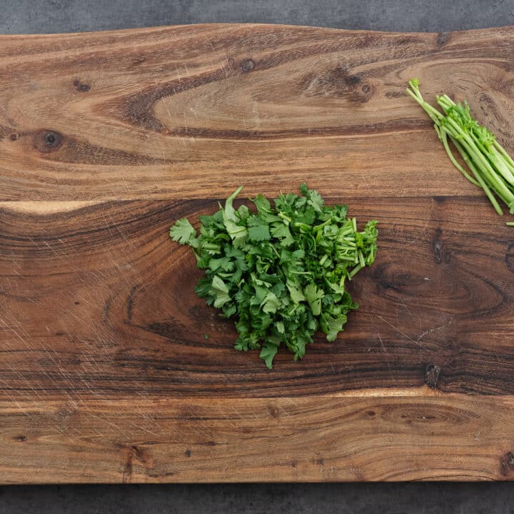 A wooden board with chopped cilantro leaves.