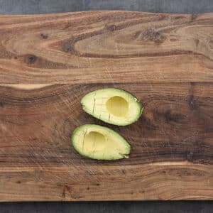 A wooden board with avocado sliced open to scoop out the flesh.